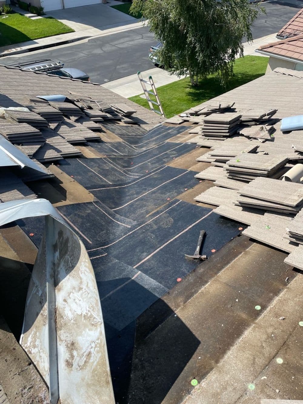 Roof repair in progress with shingles removed, showing roofing underlayment and tools.