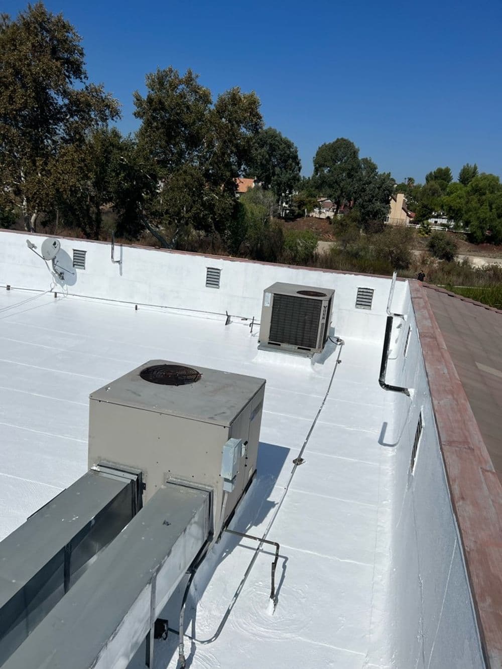 Roof with HVAC units and ventilation ducts under a clear blue sky.