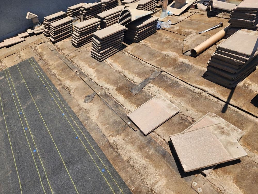Roofing project with stacked tiles, underlayment, and tools on the surface.