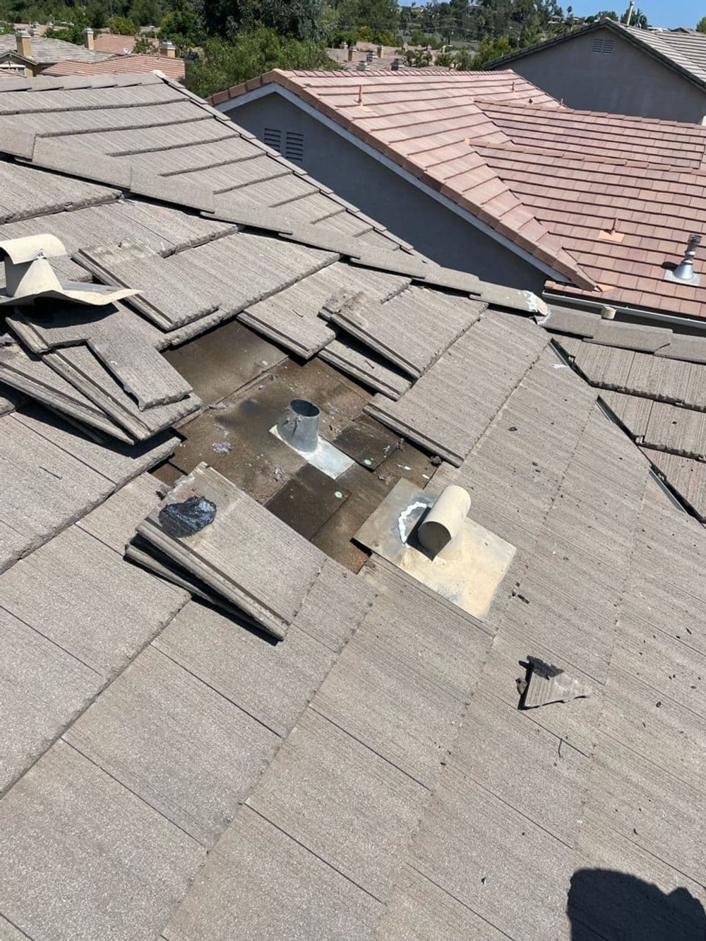 Damaged roof shingles with metal vent pipe on residential building.