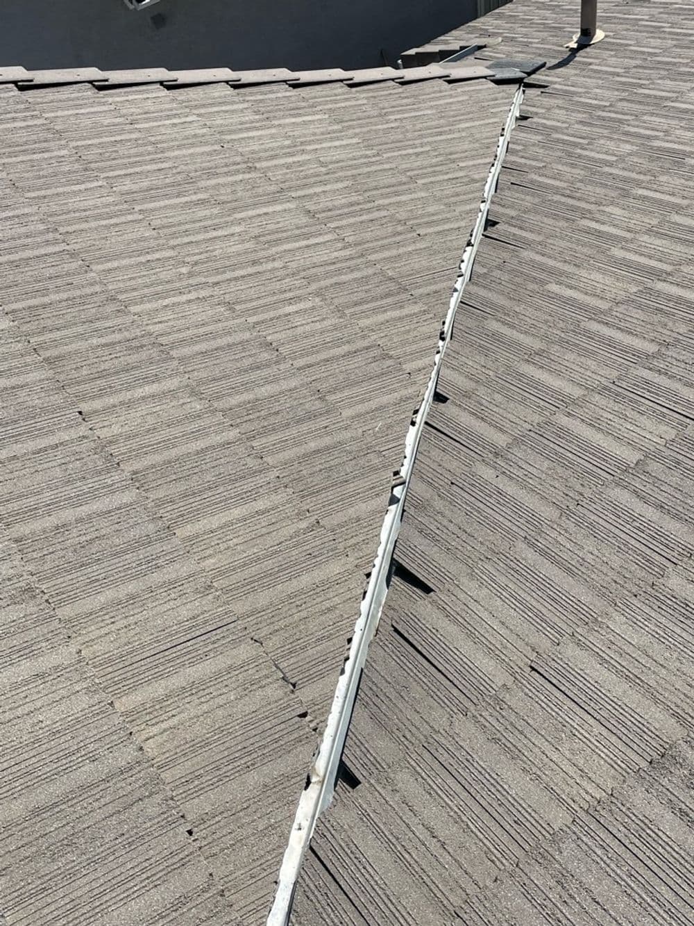 Roof detail showing joint flashing on a grey shingle surface under direct sunlight.