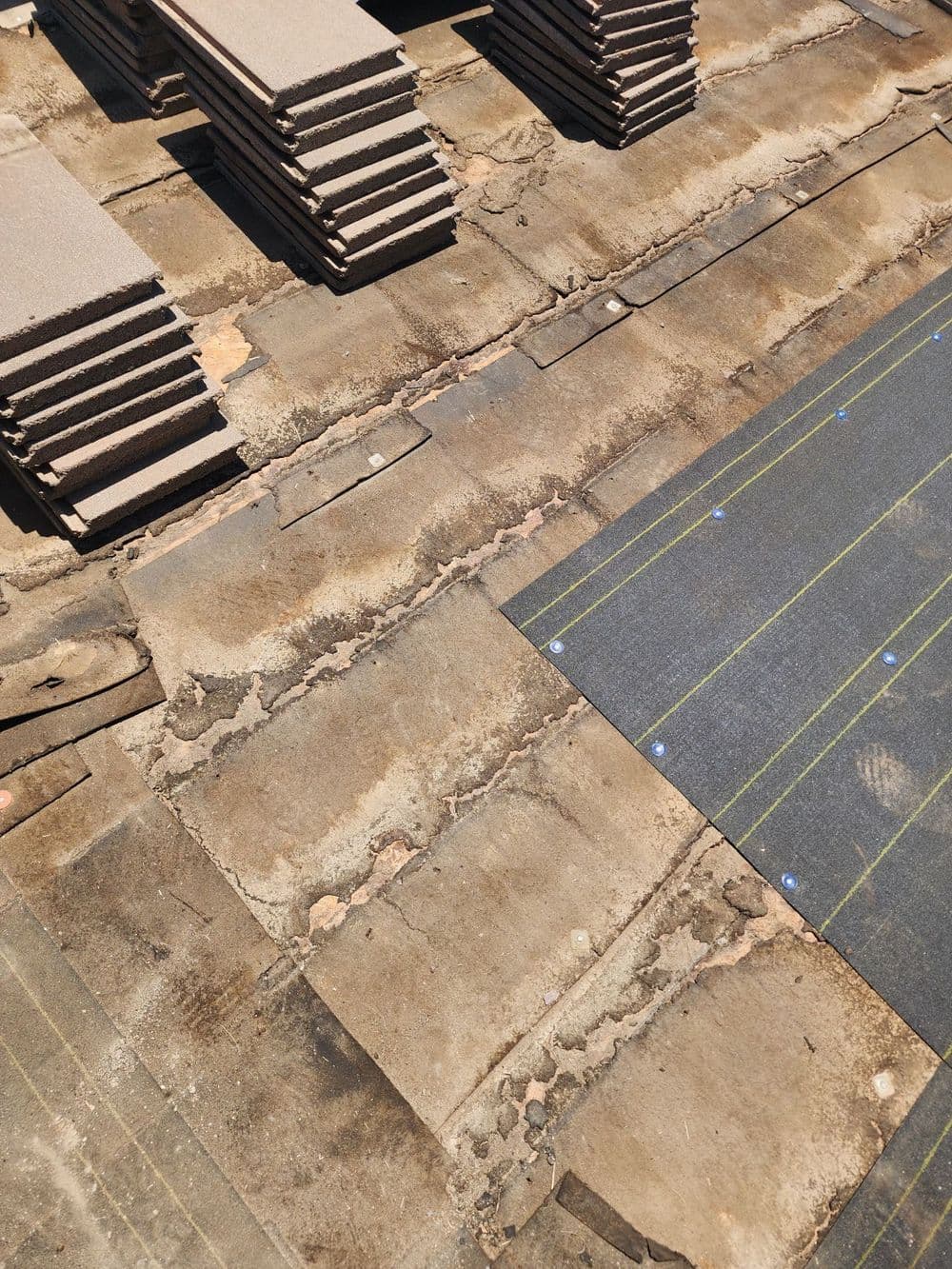 Flat roofing materials stacked on an unfinished roof with tar paper installation visible.