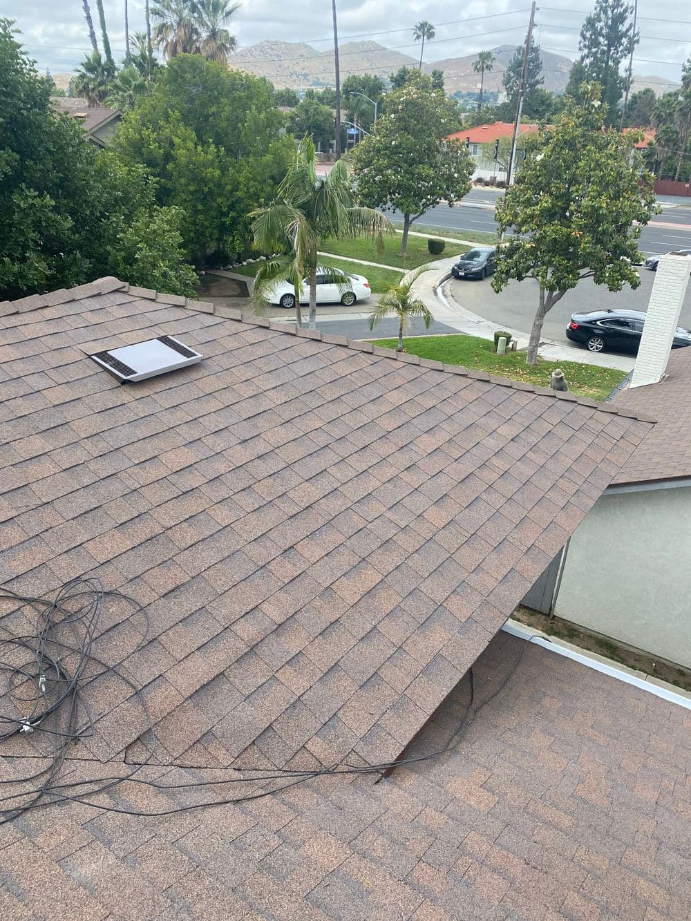 Aerial view of a shingled roof with a solar vent and surrounding trees and streets.