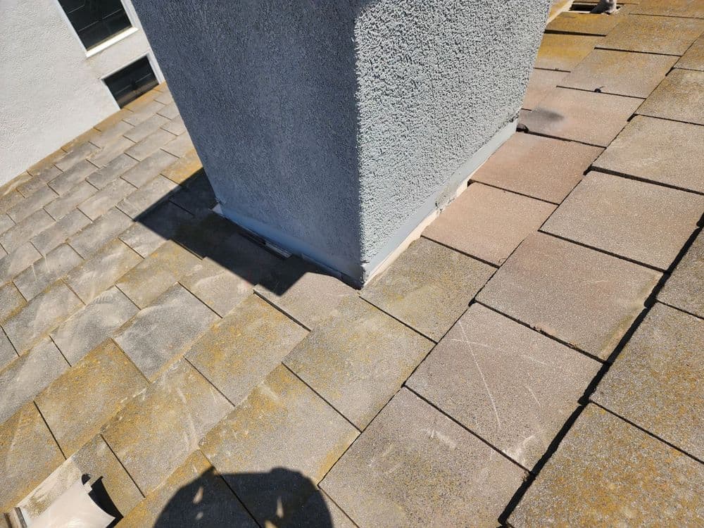 Roof shingles with a chimney and flashing detail in a sunny outdoor setting.