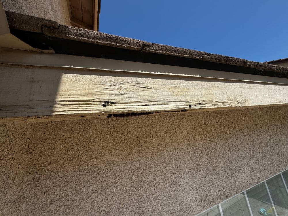 Rotting wood fascia board on a house under a clear blue sky, showing signs of water damage.