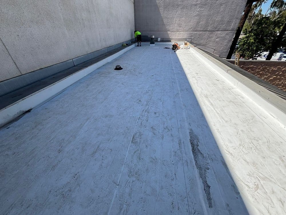 Flat rooftop installation with a worker applying materials under bright sunlight.