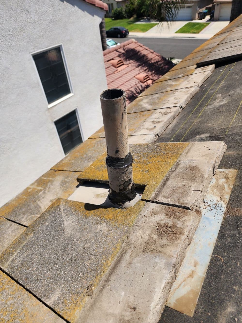 Roof plumbing vent pipe on a sloped tile roof with surrounding debris and sunlit shingles.