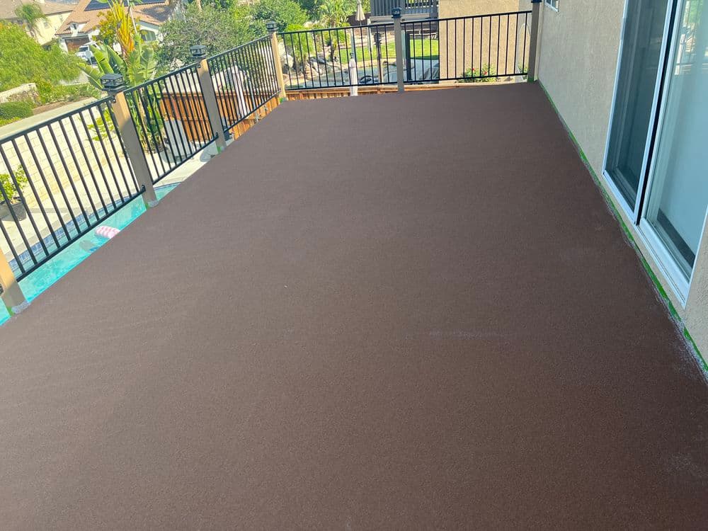 Newly resurfaced outdoor deck with brown finish and railing overlooking a landscaped area.