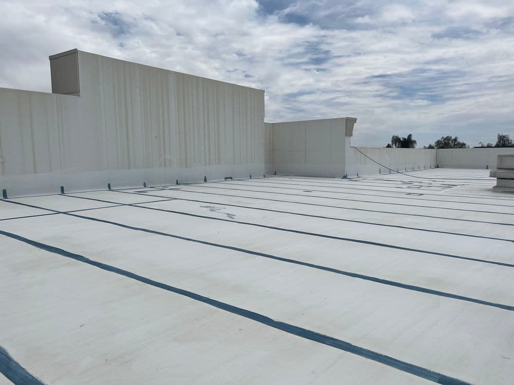 Flat rooftop with white coating and blue lines under a cloudy sky.