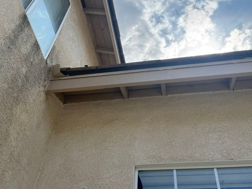 Exterior corner of a house showing eaves and cloudy sky above.